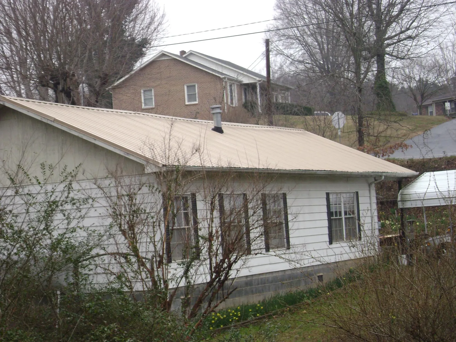 Tan metal roof on a white sided house set into a hillside — Commercial Roofing by Roofing Brothers in American Canyon